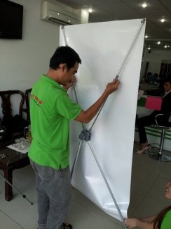 Ngoài việc là nhà phân phối standee các loại giá rẻ tại thị trường TPHCM, dịch vụ in standee trọn gói từ In Kỹ Thuật Số giúp bạn chuẩn bị chương trình sự kiện, chương trình khuyến mãi của mình tiện lợi nhất | Nhân viên In Kỹ Thuật Số hướng dẫn lắp mẫu standee nhôm trưng bày poster cho khách hàng.
