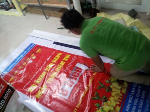 Nhân viên In Kỹ Thuật Số đang tiến hành gia công poster xuân Hiflex treo giá standee cho khách hàng